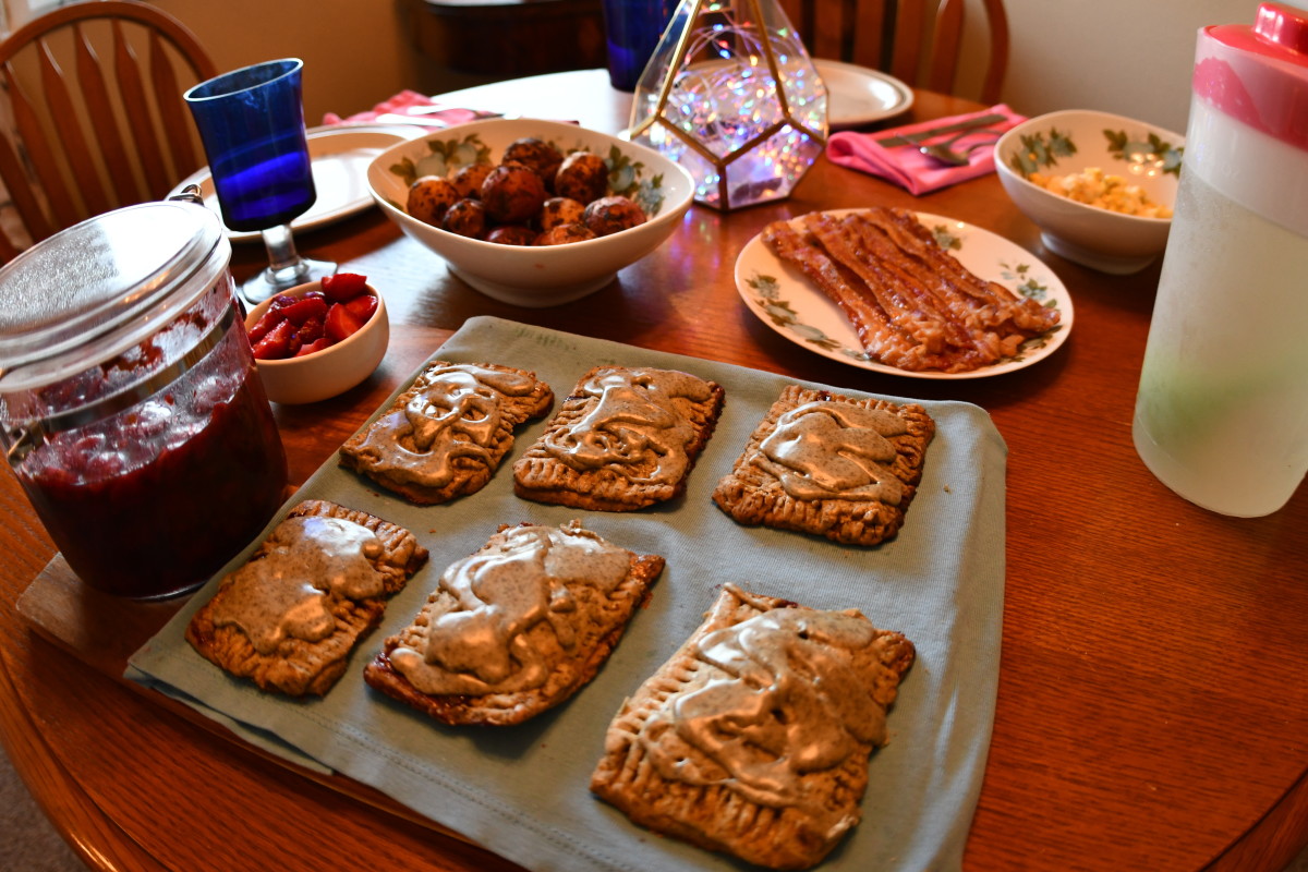 Green tea and elderberry pop tarts on a board with a blue cloth underneath. There is a table of breakfast foods and dishes.