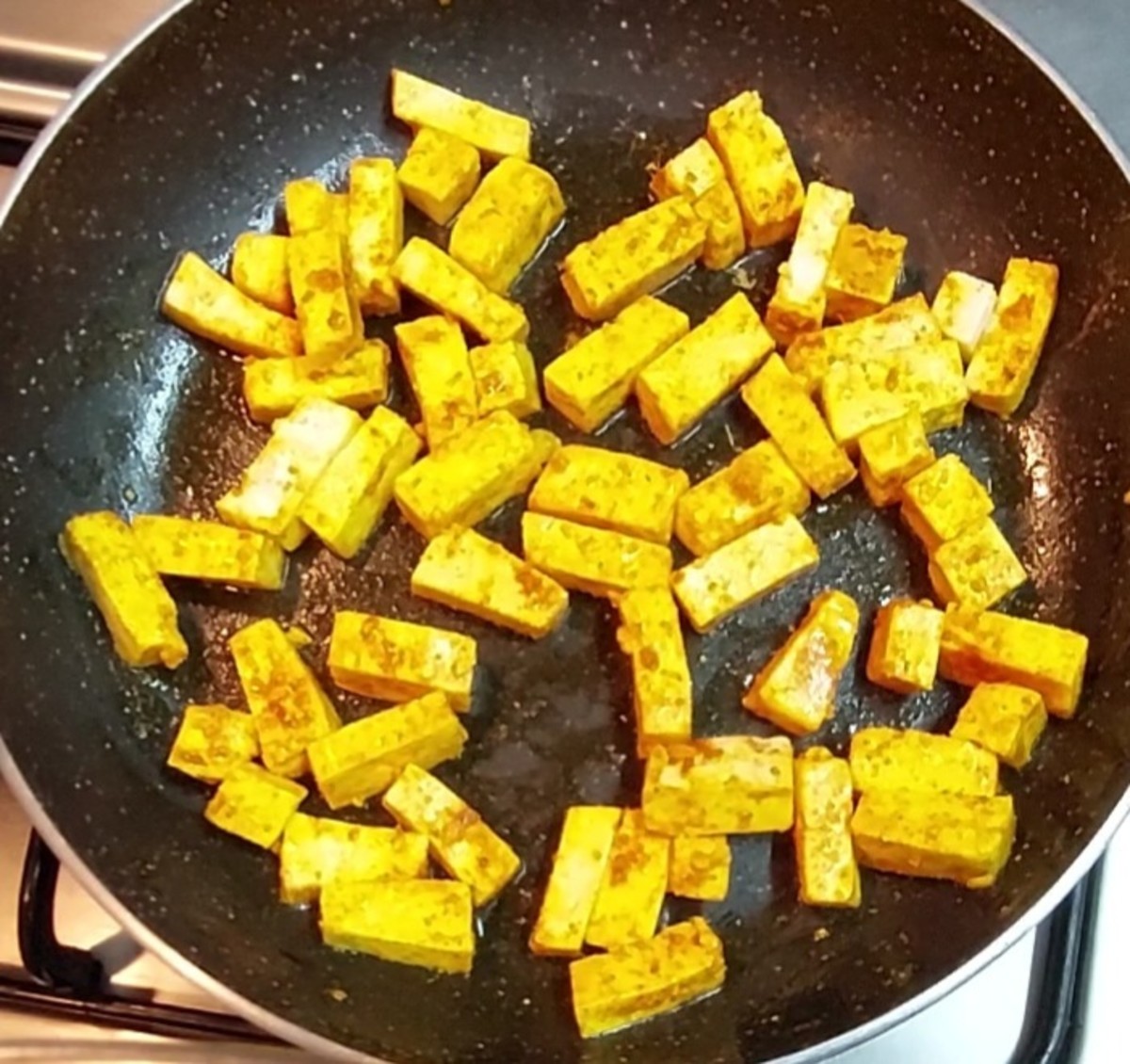 Meanwhile, heat 1 1/2 teaspoon ghee in a frying pan, spreading the ghee all over the pan. Add cubed paneer pieces. Add 1/4 teaspoon turmeric powder, 1/2 teaspoon red chili powder and mix to coat paneer with spices.