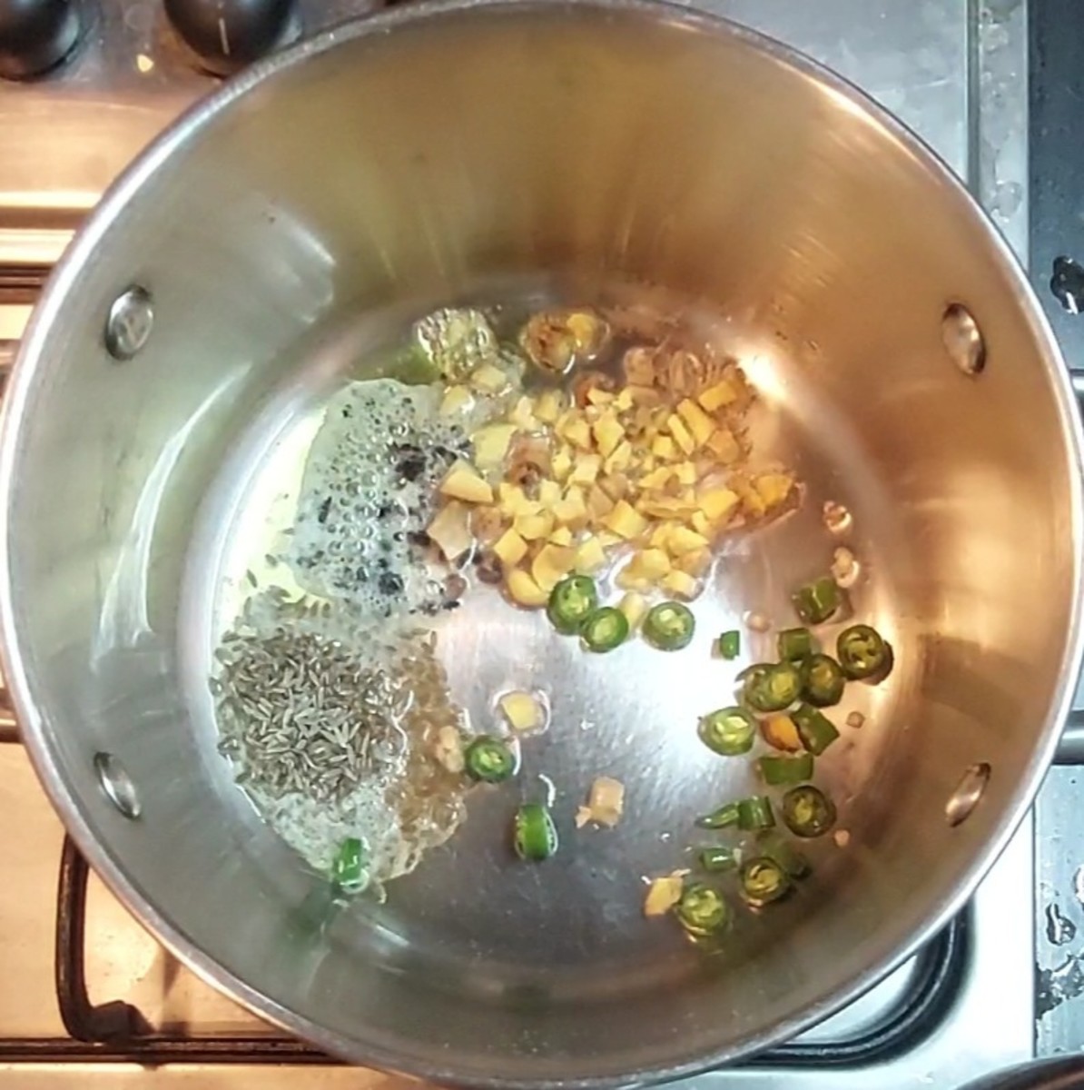 In a pan, heat 1 teaspoon ghee and 1 teaspoon oil. Splutter 1 teaspoon cumin seeds. Add 1/2 teaspoon coarsely crushed black pepper, 2 inches long chopped ginger, 1-2 chopped green chilies and a sprig of curry leaves. Saute for a few seconds.