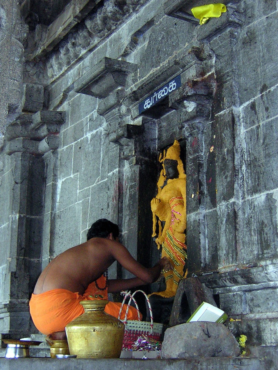 A 'pujari' adorns the stone statuette of Goddess Durga outside a temple in Kanchipuram with yellow turmeric paste.