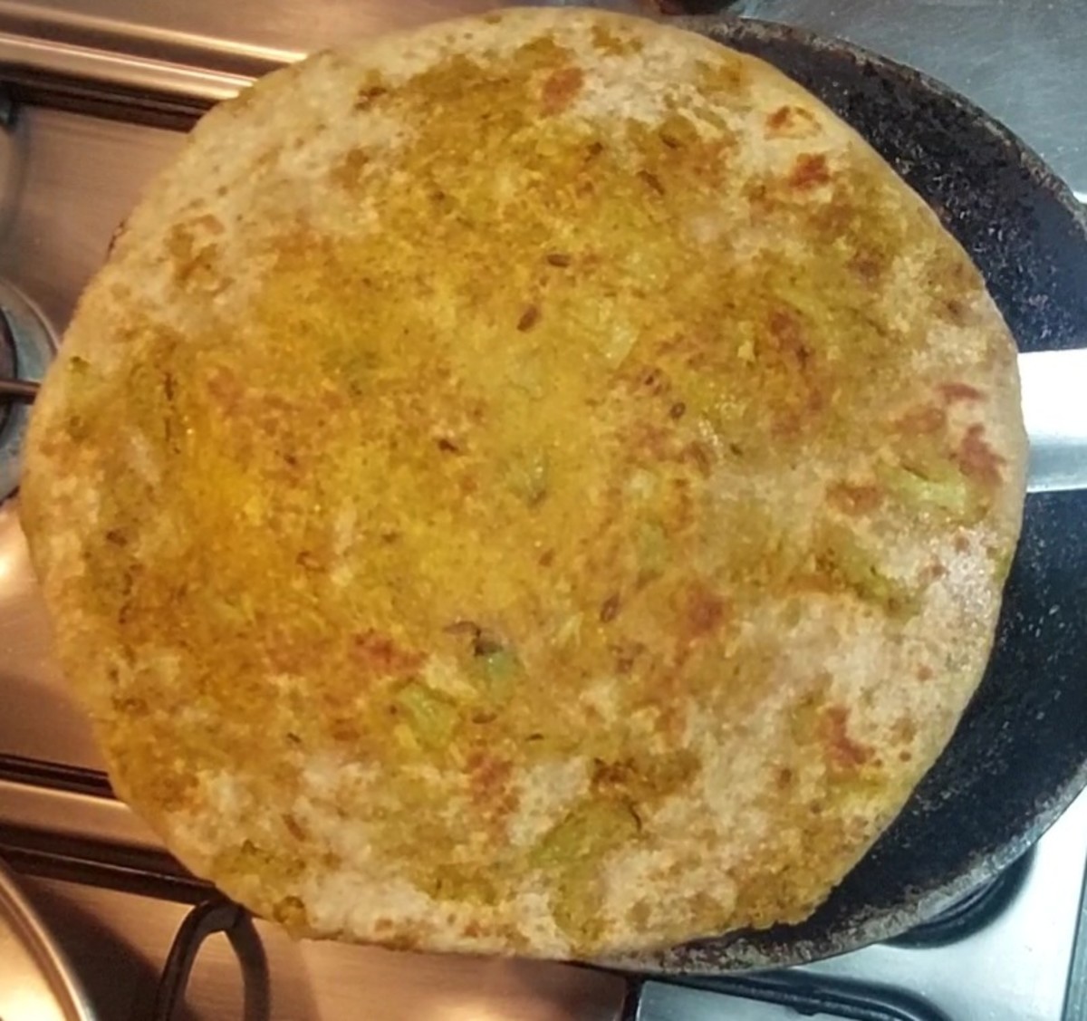 Heat a tawa, drizzle a few drops of ghee on the tawa, add rolled paratha, and cook. Drizzle a few more drops of ghee on the paratha. Flip and cook the other side till brown spots appear. Add more ghee if required.