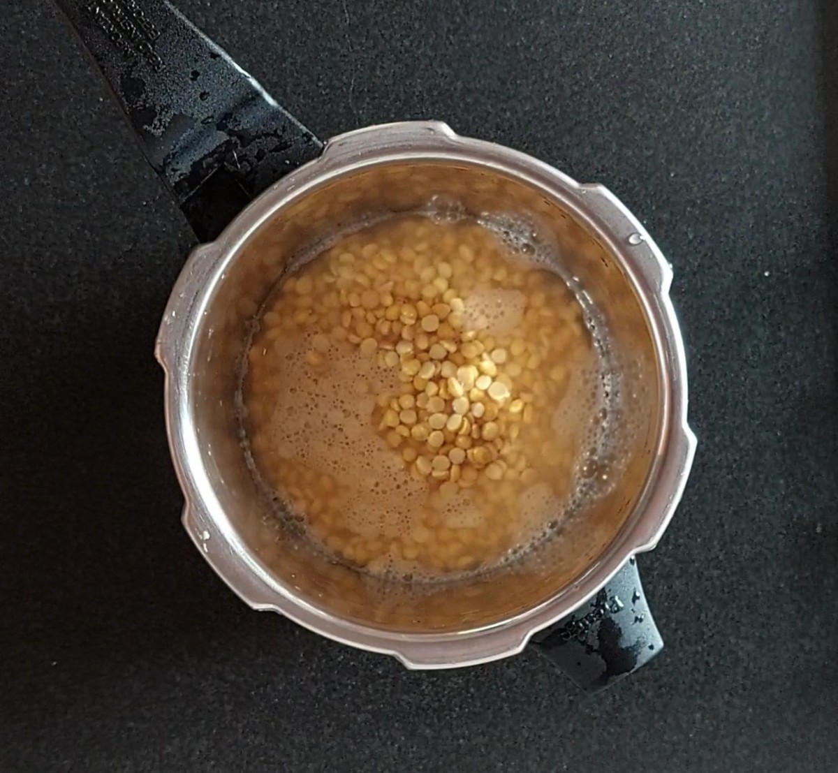 After soaking, transfer the chana dal to a cooker along with the soaking water. Close the lid and take 3 whistles over medium flame.