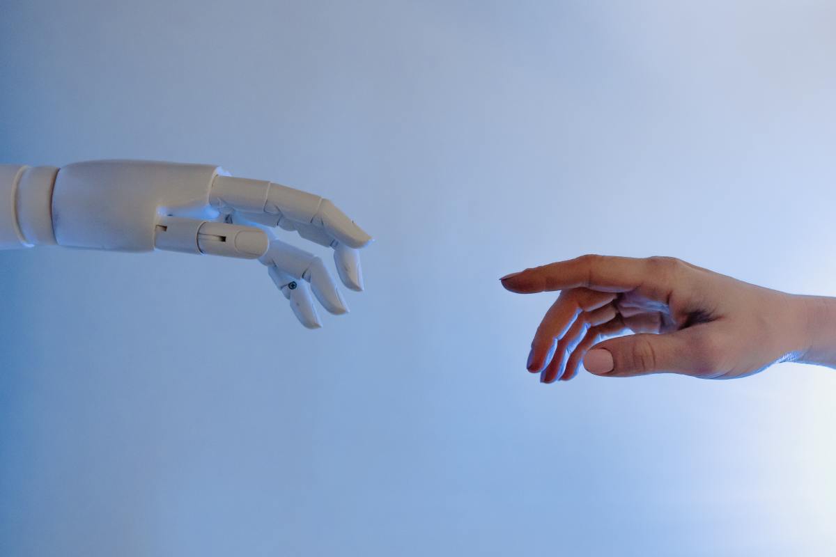 A robotic hand and a human hand touching at the finger tips. 