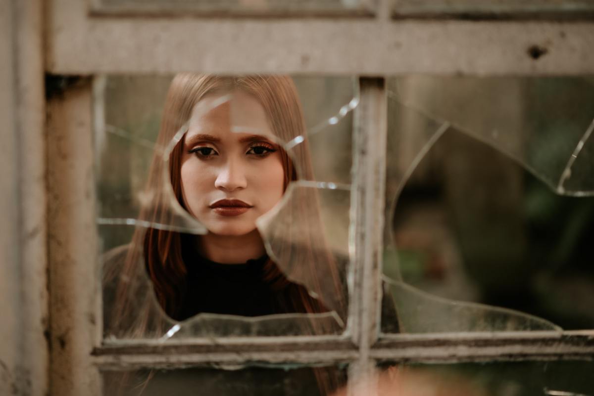 A woman stares through a broken window. Broken window theory is a popular idea in addressing crime, and it can also be applied in the workplace.