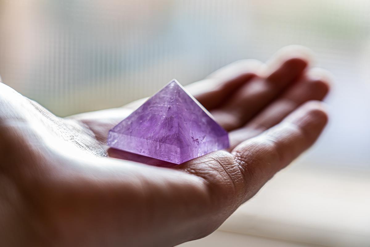 Amethyst crystal sits in a palm of a person's hand.