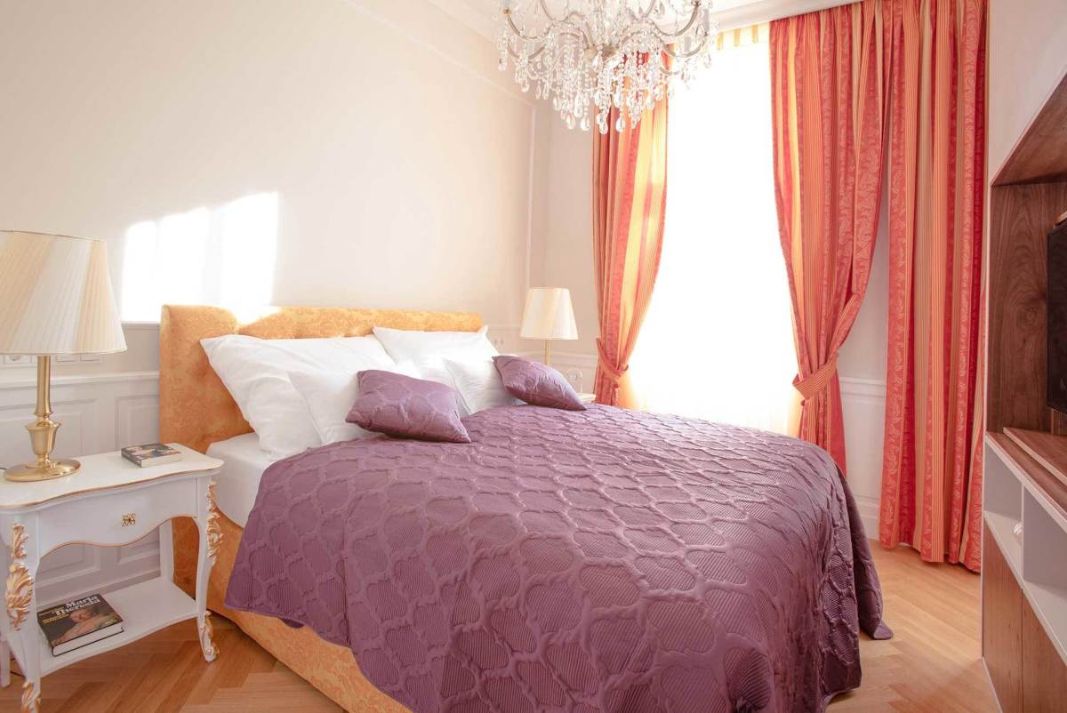 You don't need to go overboard in the bedroom to create a style. For the Goat, try a mauve bedspread that isn't overwhelming but rather calming. Soft red curtains and an orange-hued headboard give the room a unique feel. A chandelier is classy.