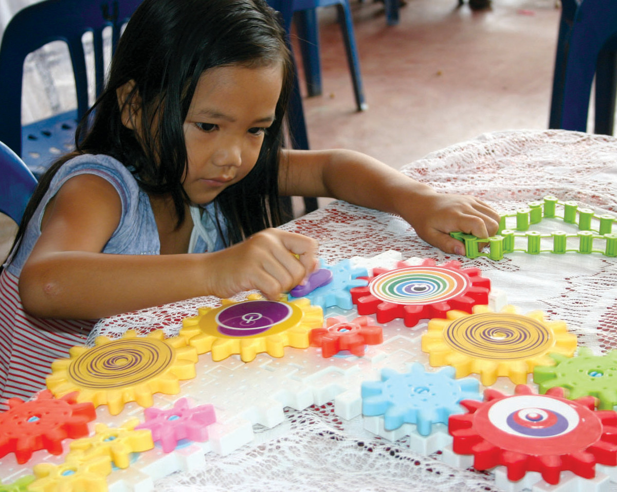 A young girl in Laos plays with toy gears. Gears are an excellent STEM toy.