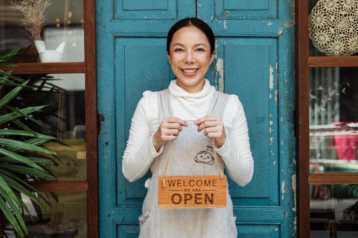A woman holds an "Open" sign in front of a wooden door. Are you open to reimagining your career?