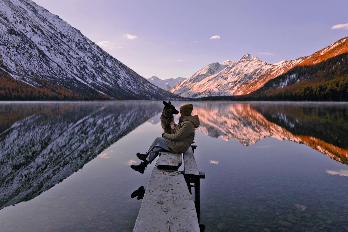 Woman sitting on dock with dog by a lake overlooking mountains.